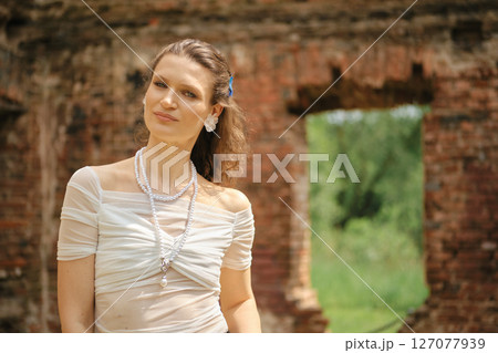 Beautiful woman poses gracefully in a vintage dress among rustic ruins on a sunny day 127077939