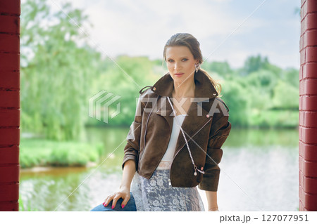 Stylish woman poses by serene lake in a green park during a sunny day 127077951