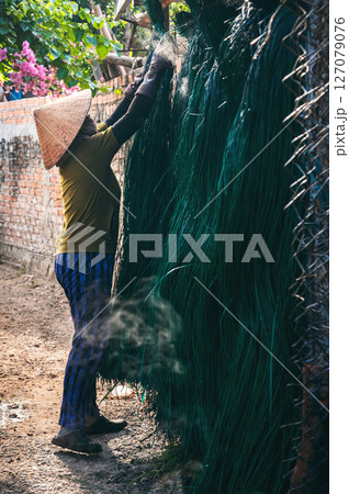 Vietnamese woman in traditional straw hat dries dyed reeds at a woven mat factory in village in Vietnam Vietnamese woman in traditional straw hat dries dyed reeds at a woven mat factory in village in Vietnam 127079076