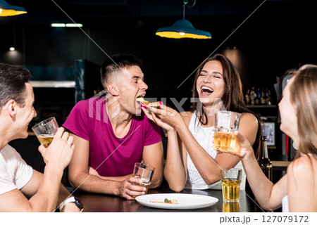 Cheerful friends in the pub. Drinking beer, eating pizza, talking, having fun. 127079172