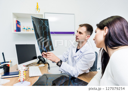 Traumatologist showing MRI film to patient in hospital. Traumatologist showing MRI film to patient in hospital. 127079254