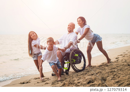 Disabled man in a wheelchair with his family on the beach. 127079314