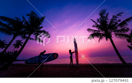 Silhouette of surfers couple holding long surf boards at sunset 127079491
