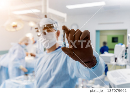 Spinal surgery. Surgeon show polyaxial screw in operating room Spinal surgery. Surgeon show polyaxial screw in operating room 127079661