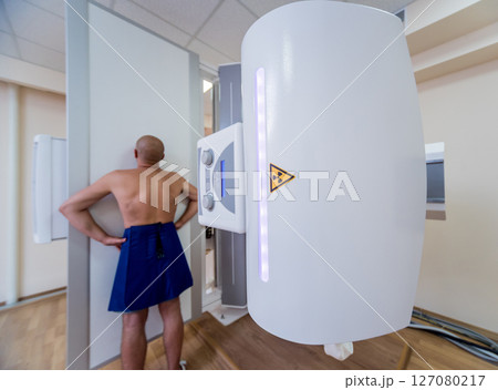 Radiologist and patient in a x-ray room. Classic ceiling-mounted x-ray system. 127080217