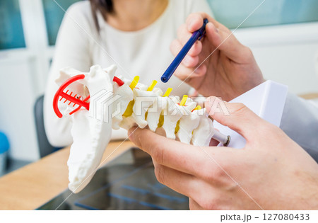 Orthopedist showing spine model to patient in hospital Orthopedist showing spine model to patient in hospital 127080433