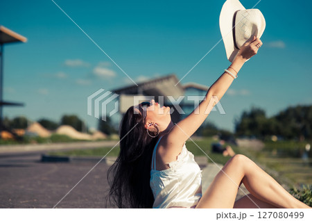 The slender girl is sitting on the warm soil, shielding her eyes from the sun with stylish glasses The slender girl is sitting on the warm soil, shielding her eyes from the sun with stylish glasses 127080499