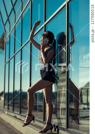 The young woman near the glass building stopped talking, holding the phone to her ear The young woman near the glass building stopped talking, holding the phone to her ear 127080518