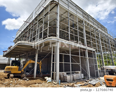 A yellow excavator is in front of a building under construction A yellow excavator is in front of a building under construction 127080740