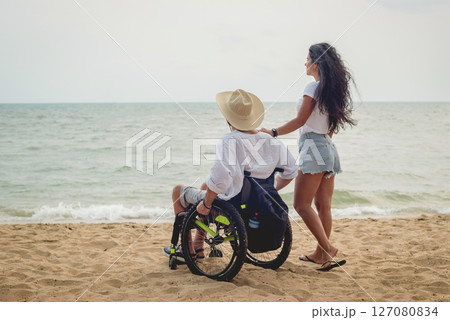 Disabled man in a wheelchair with his wife on the beach. Disabled man in a wheelchair with his wife on the beach. 127080834