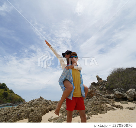 A young couple are leisurely walking along the beach, holding hands and enjoying the warm sun A young couple are leisurely walking along the beach, holding hands and enjoying the warm sun 127080876