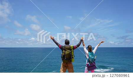 A young couple are hiking on a rugged rocky cliff that offers a view of the ocean 127080961