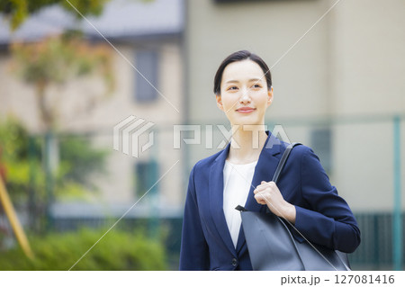 住宅街を歩くスーツを着た若い女性 127081416