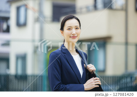 住宅街を歩くスーツを着た若い女性 127081420