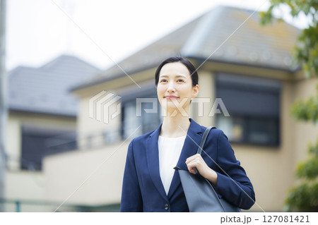 住宅街を歩くスーツを着た若い女性 127081421
