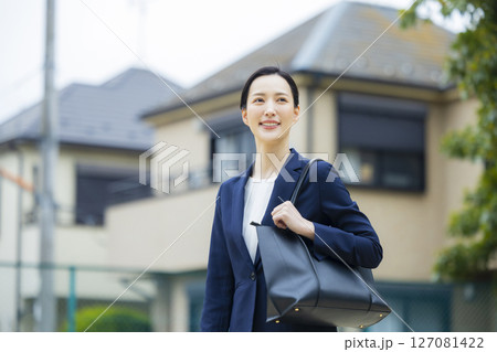 住宅街を歩くスーツを着た若い女性 127081422