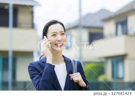 住宅街を歩くスーツを着た若い女性 127081424