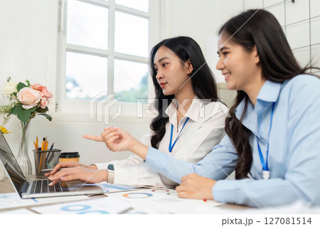 Teamwork and Engagement. Women collaborating on a laptop in a bright office setting. Teamwork and Engagement. Women collaborating on a laptop in a bright office setting. 127081514