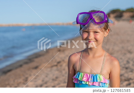 Young girl in colorful swimsuit with snorkeling goggles smiling on a sunny beach Young girl in colorful swimsuit with snorkeling goggles smiling on a sunny beach 127081585