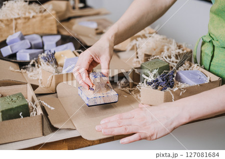 Person stamps kraft packaging near handmade soaps, dried lavender, and eco-friendly filler. Visual identity for makers, slow brand values, minimalist packaging, artisanal design 127081684