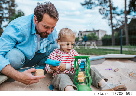 Father and little toddler son playing in the sandbox on playground. 127081699