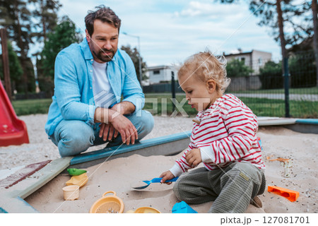Father and little toddler son playing in the sandbox on playground. Father and little toddler son playing in the sandbox on playground. 127081701