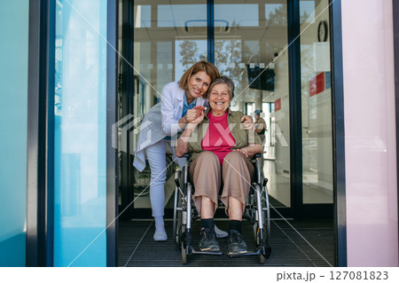 Elderly patient in wheelchair and female physician smiling at clinic. Elderly patient in wheelchair and female physician smiling at clinic. 127081823