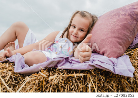 A cute little girl is lying on a straw bed covered with a purple bedspread A cute little girl is lying on a straw bed covered with a purple bedspread 127082852