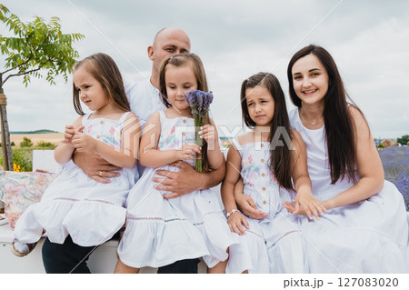 A family sits on a white retro bench in a blooming field A family sits on a white retro bench in a blooming field 127083020