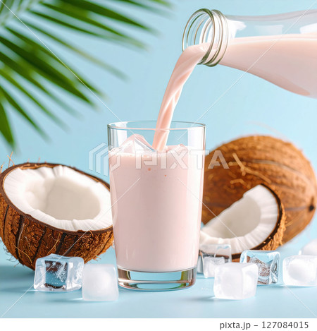 Creamy pink coconut smoothie is poured into glass with ice cubes, surrounded by fresh coconuts on blue background 127084015