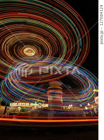 Long exposure circular light patterns created by spinning carnival ride against dark night sky at summer fairground 127084124