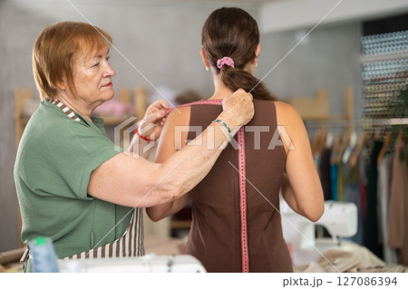 Mature woman seamstress takes measurements from a girl Mature woman seamstress takes measurements from a girl 127086394