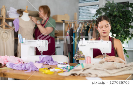 Female seamstress working on a typewriter against the background of a dressmaker and a mannequin Female seamstress working on a typewriter against the background of a dressmaker and a mannequin 127086703