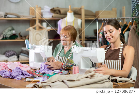 Elderly and young women seamstresses sewing on machine 127086877
