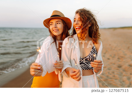 Beautiful Two women holding sparkler celebration on beach. They are having a great time together! 127087515