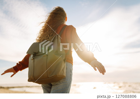 As she walked along the beach, the woman tourist adjusted her backpack, taking in the salty sea air 127088806