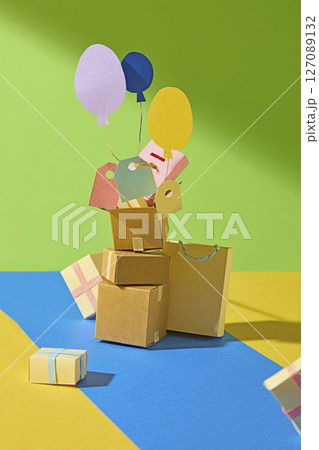 Front view of cardboard boxes, shopping bags, price tags and decorative balloons on a colorful background, ideal for promoting discounts and commercial campaigns in a modern, playful visual style. 127089132