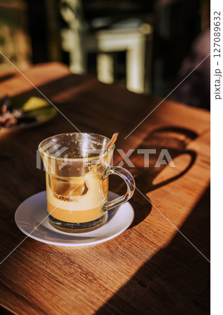 Calm morning. Still life of empty coffee cup. Empty glass coffee cup with milk foam remnants sits in sunlight on wooden cafe table, casting a soft shadow. Concept of coffee break, cozy moment 127089632