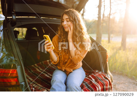 Young woman enjoys a sunny day outdoors while sitting in her car. Travel, weekend, nature, relax 127090029