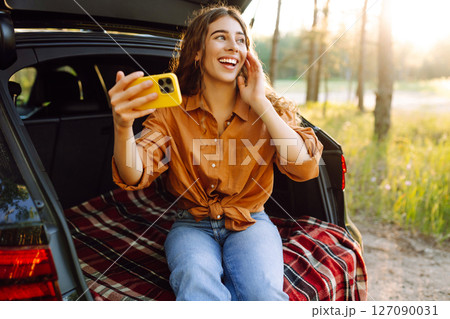 Happy Woman is resting in trunk of car and taking selfie. Selfie time. Lifestyle, travel 127090031