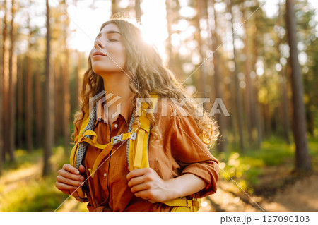 Tourist woman hiking alone in thick autumn forest. Stylish female looks for pathway among trees. 127090103