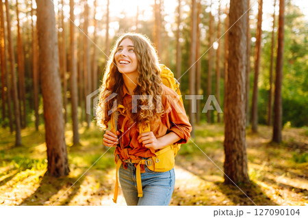 Tourist woman hiking alone in thick autumn forest. Stylish female looks for pathway among trees. 127090104