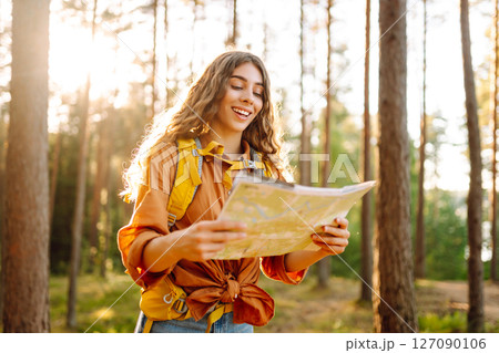 A traveler woman stands in a lush forest, examining a map with a focused expression 127090106