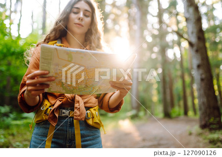 A traveler woman stands in a lush forest, examining a map with a focused expression 127090126