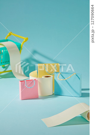Cute paper cut shopping bags with mini bill rolls on blue background express the rush of online shopping and limited-time deals. Creative photography with shopping concept Cute paper cut shopping bags with mini bill rolls on blue background express the rush of online shopping and limited-time deals. Creative photography with shopping concept 127090664