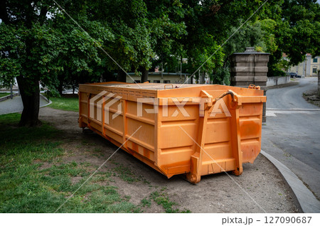 Large orange industrial dumpster placed under trees in urban park area outdoors Large orange industrial dumpster placed under trees in urban park area outdoors 127090687