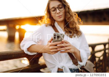Young woman using her smartphone while walk on embankment. Concept of blogging, technology, weekend. Young woman using her smartphone while walk on embankment. Concept of blogging, technology, weekend. 127091031