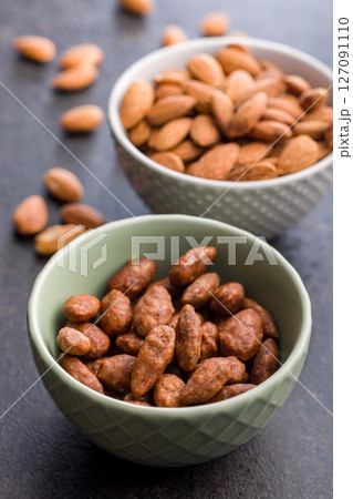 Almond nuts coated in sugar and honey in bowl on black table. Almond nuts coated in sugar and honey in bowl on black table. 127091110
