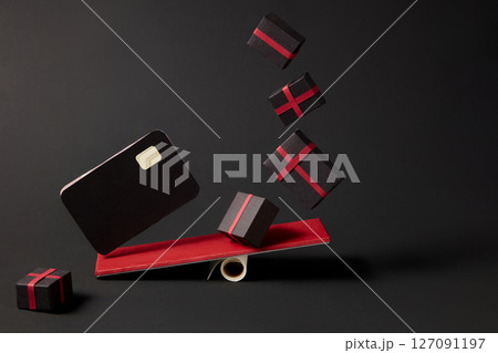 Gift boxes and ATM cards are playing seesaw on minimalist black background. Represents online orders, digital sales or festive e-commerce delivery. 127091197
