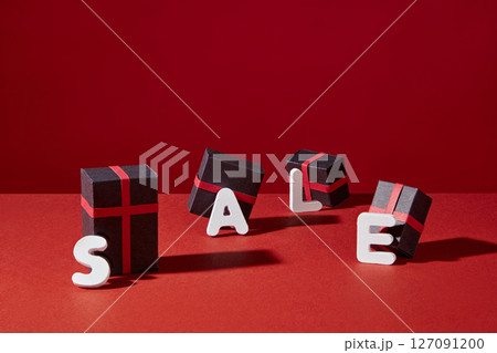 On a red background, small black fruit boxes with red ribbons, attached with a letter, combine to form the message "sale". Image for black friday design, big sale programs 127091200